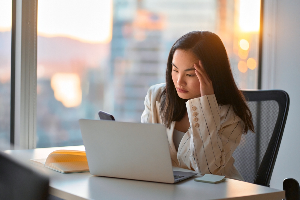 A stressed-out woman looks at her computer and her phone.